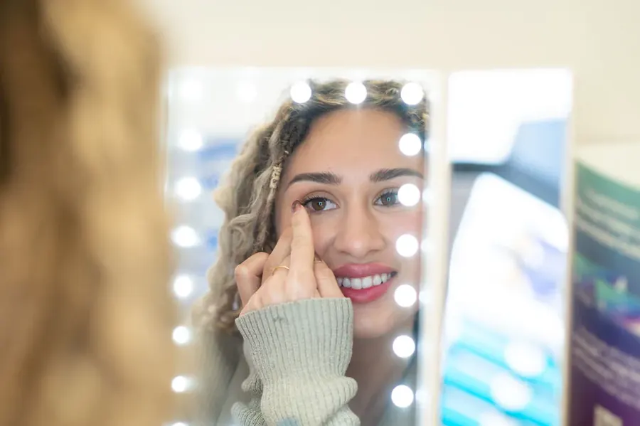 A patient practicing contact lens insertion at a lighted mirror at TSO Kyle