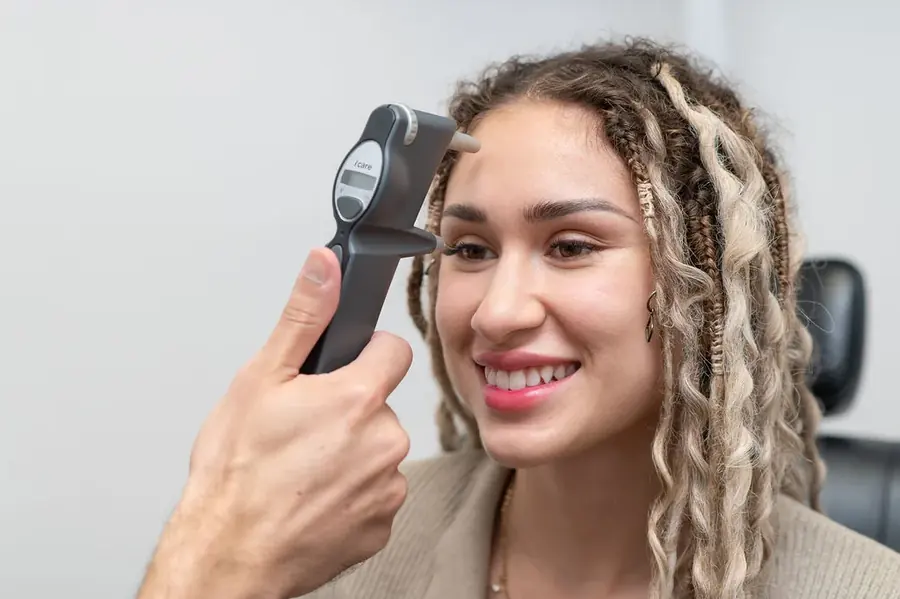 An eye doctor checking a smiling patient's eye pressure with a handheld iCare tonometer